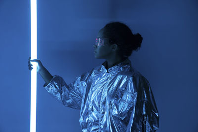 Young woman holding illuminated neon light against blue background