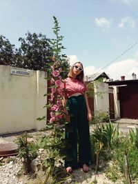 Young woman standing by plants against sky
