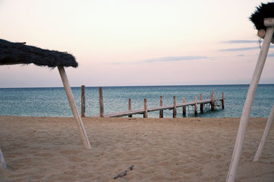 Scenic view of wooden pier at sandy beach against sky