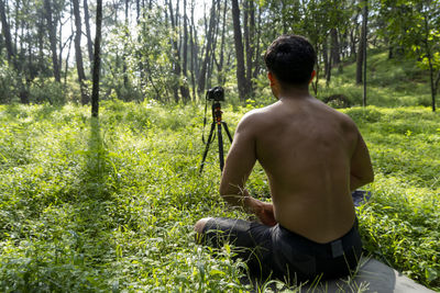 Young man practicing yoga asana, balance, meditating while standing on one leg on sports mat on gree