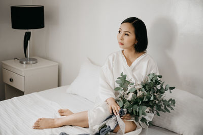 Young woman looking down while sitting on white wall