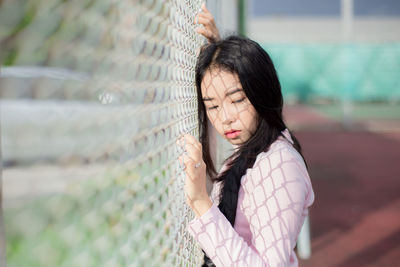 Side view of thoughtful young woman looking away by net at court