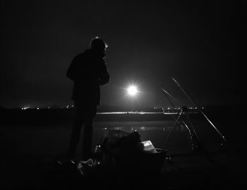 Silhouette man standing on illuminated street against sky at night