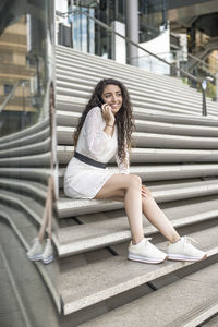 Young woman talking on phone sitting on steps outdoors