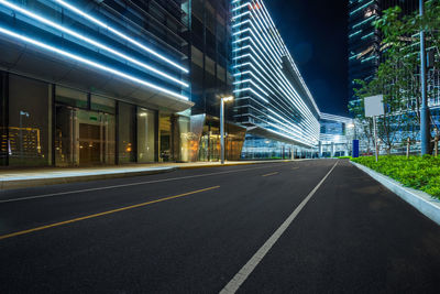 Road by illuminated buildings in city at night