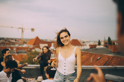 Smiling young woman sitting outdoors against sky in city