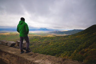 A man traveling on foot, standing in a bright jacket on top of one of the mountains, looking into