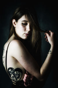 Young woman with tattoo standing against black background