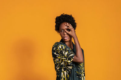 Young african american woman with short hair dressed in a summer shirt posing on an orange colored