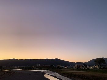 Road amidst field against clear sky during sunset