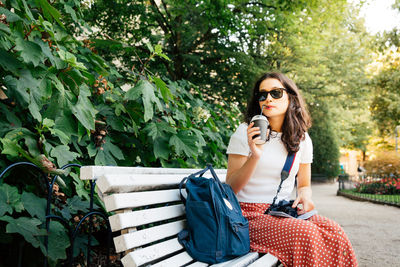 Woman having drink while sitting on bench at park