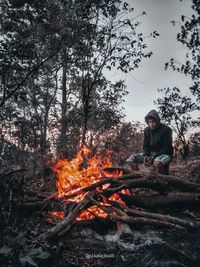 Young man sitting by bonfire in forest