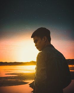 Side view of young man standing at beach against sky at night