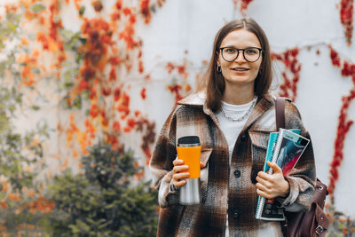 Portrait of young woman holding drink standing outdoors