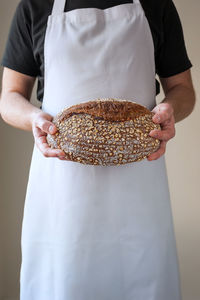 Close-up at bakers hands holding a loaf of organic sourdough bread in front of him.