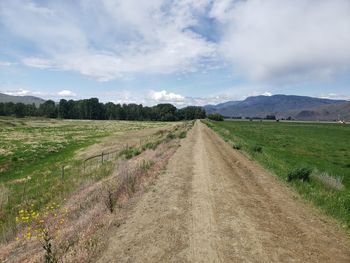 Dirt road amidst field against sky