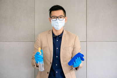 Portrait of man holding sanitizer and standing against wall