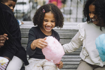 Cheerful girl having fun with siblings while holding cotton candy at amusement park
