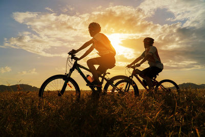 Men riding bicycle on field against sky during sunset