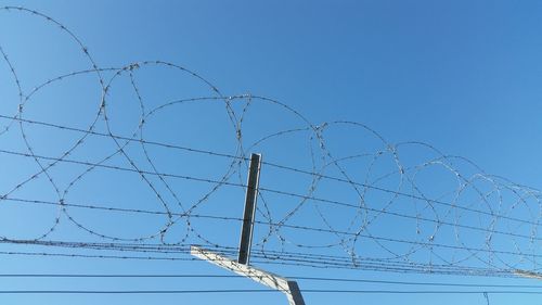 Low angle view of barbed wire on fence against clear blue sky