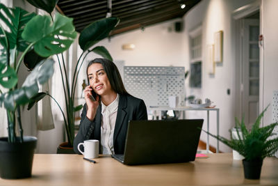 Smiling employee speaking on smartphone at desk with laptop