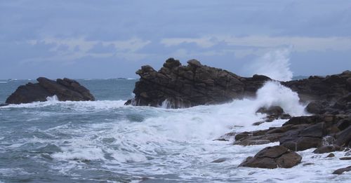 Waves splashing on rocks at shore against sky in brittany