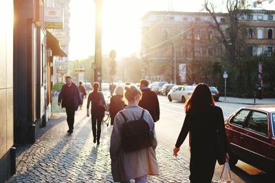 People walking on sidewalk in city against bright sun