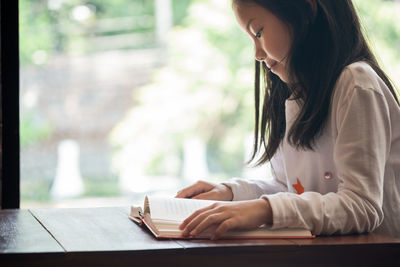 Side view of smiling girl reading book in desk at home