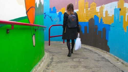 Rear view of woman walking in alley amidst graffiti walls