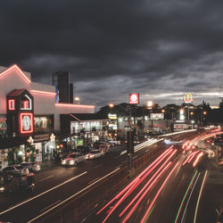 Light trails on road in city against cloudy sky