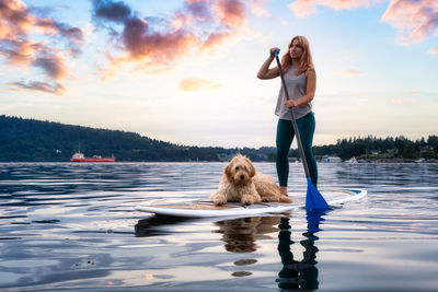 Woman with dog at beach against sky during sunset