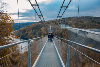 People walking on footbridge against sky