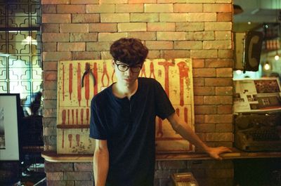 Young man wearing eyeglasses while standing against brick wall