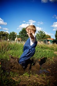 Full length of boy splashing mud on field against sky