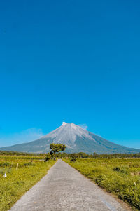 Road leading towards mountain against blue sky