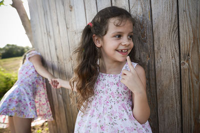 Smiling girl holding sister hands while standing against wooden fence