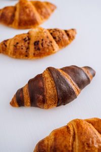 Close up of bunch of delicious brown and chocolate croissants laid out on a white table	
