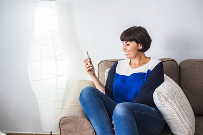 Young woman using phone while sitting on sofa at home