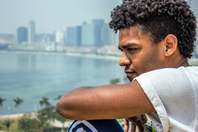 Thoughtful young man looking away with buildings in background at city