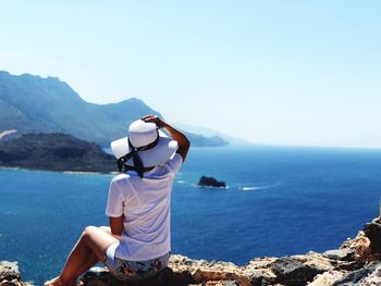 Rear view of woman sitting on shore against clear sky