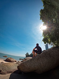 Man on rock by sea against clear blue sky