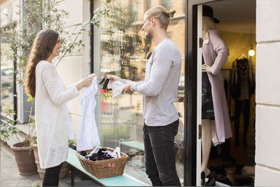 Happy male owner showing price tag of shoe to customer outside boutique