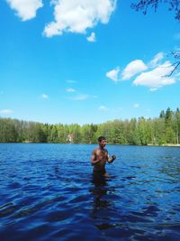 Shirtless man looking away while standing in lake against cloudy sky