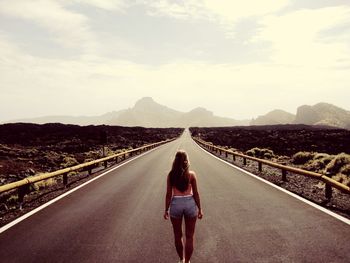 Rear view of woman walking on road against sky