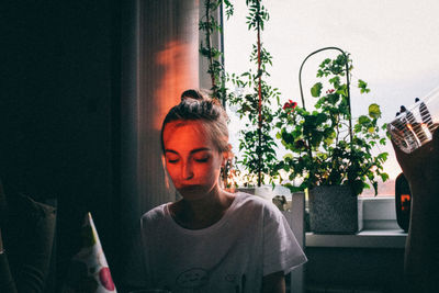 Woman looking away while sitting on potted plant at home