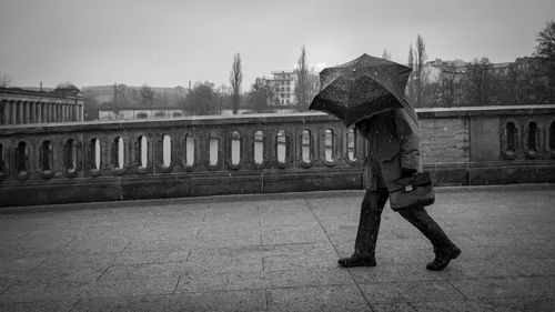 Side view of woman with umbrella walking against built structure