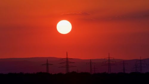 Silhouette electricity pylon against sky during sunset