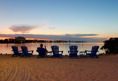 People relaxing on beach against sky during sunset