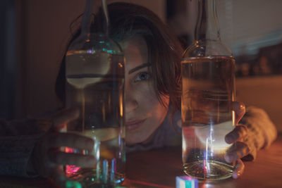 Portrait of thoughtful woman with wine bottles on table in darkroom