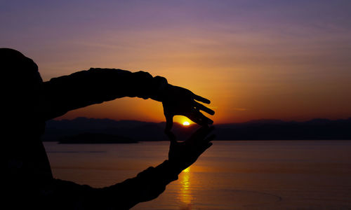 Silhouette hand holding sun over sea against sky during sunset